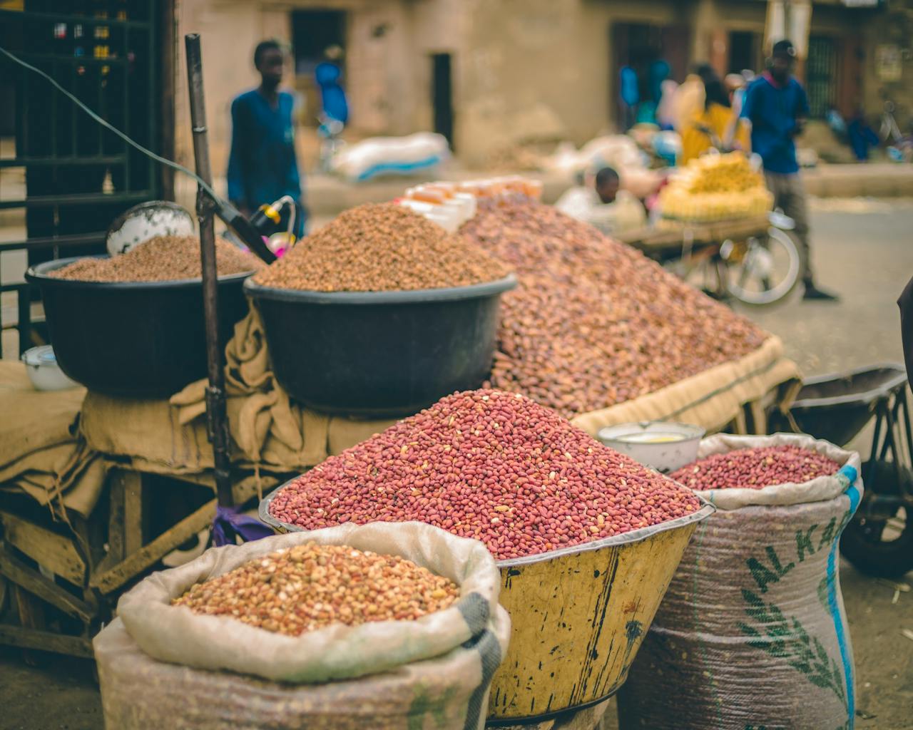 Vibrant outdoor market with various beans and legumes in sacks, bustling with activity.